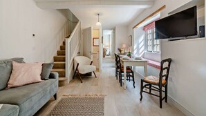 Un salon avec un canapé, une table à manger et des chaises, un escalier et un téléviseur fixé au mur.