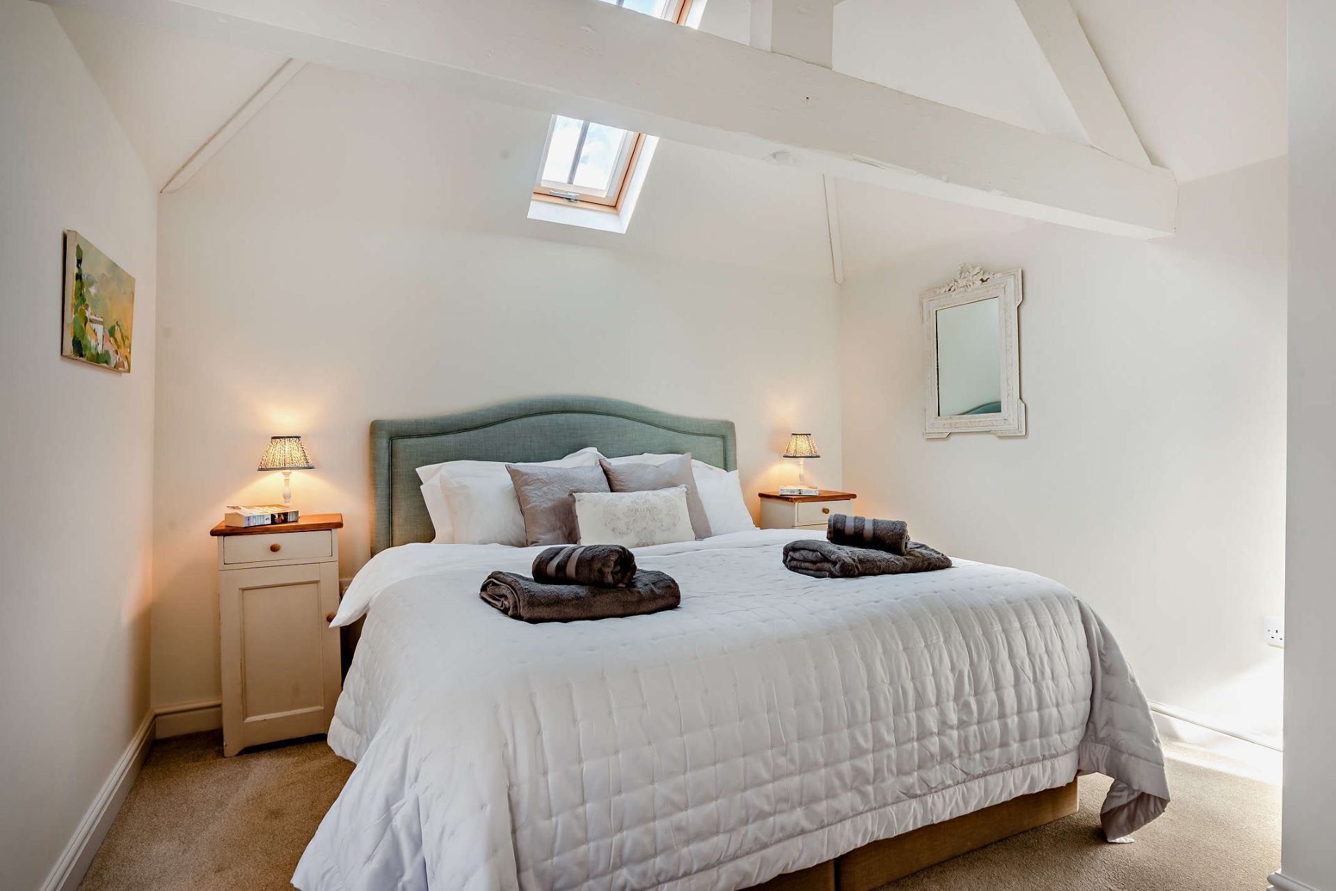 A bedroom with a bed, bedside lamps, a nightstand, a window, and a mirror.