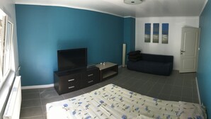 Un dormitorio con una cama, un televisor en una cómoda, un sofá y una puerta.