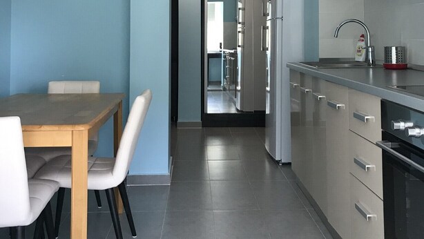 Una cocina moderna con armarios grises, un refrigerador de acero inoxidable y un comedor con mesa de madera y sillas blancas.
