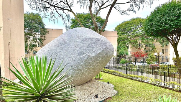 A large rock sculpture in a landscaped garden with green plants and a fence. - Apartamento Próx Tiete Plaza Shopping (São Paulo)