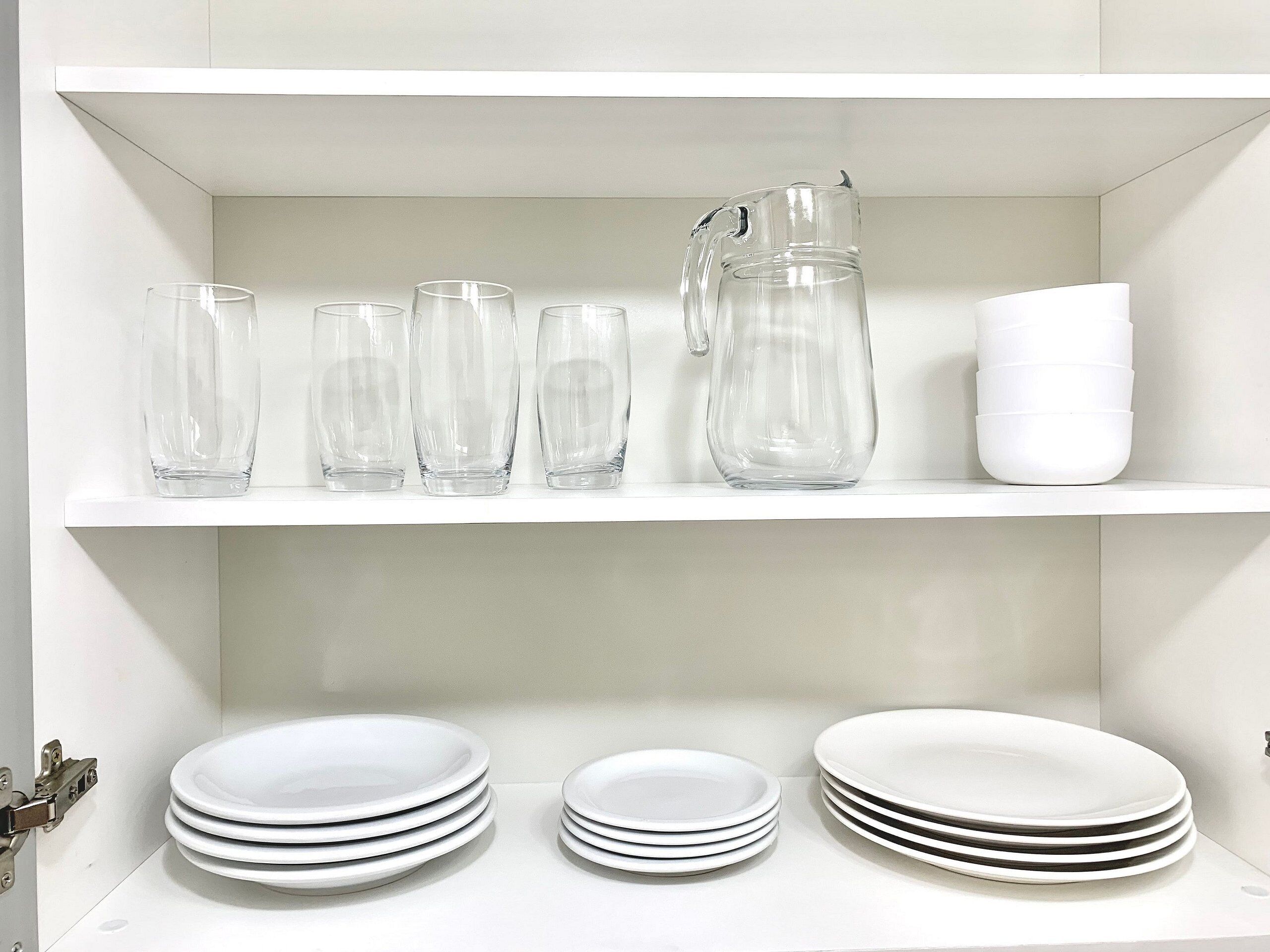 Een witte plank met glazen servies en witte borden.