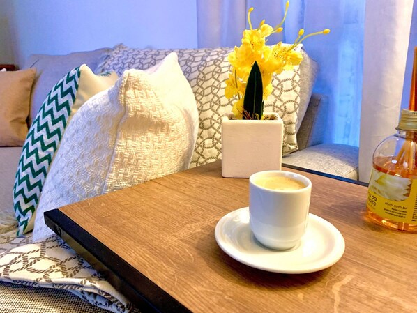 A cozy seating area with a wooden table, a white cup of coffee, a bottle of orange juice, and a potted plant with yellow flowers.