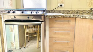 A kitchen with a stove, a chair, and wooden cabinets. - Apartamento Próx Tiete Plaza Shopping (São Paulo)