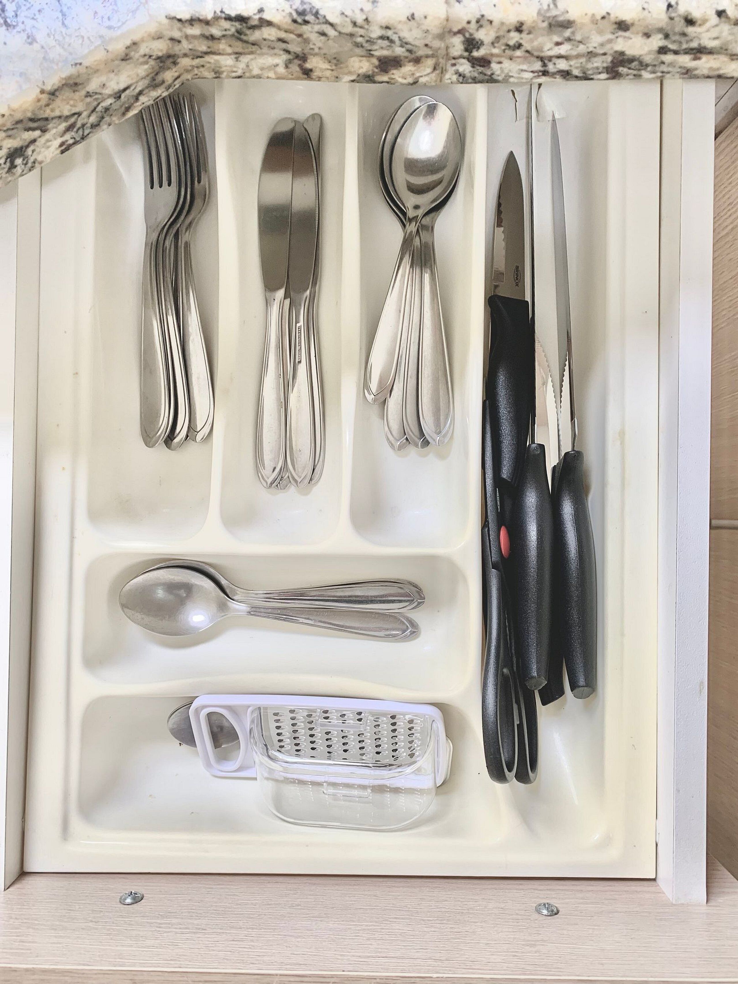 Un cajón con utensilios de cocina ordenados, incluyendo tenedores, cucharas, un cuchillo y un rallador.