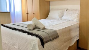 A neatly made bed with a rolled white towel, a grey and black striped blanket, and white pillows. - Apartamento Próx Tiete Plaza Shopping (São Paulo)