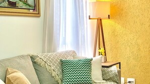 A living room with a sofa, patterned cushions, a painting on the wall, a lamp, and a window with curtains. - Apartamento Próx Tiete Plaza Shopping (São Paulo)