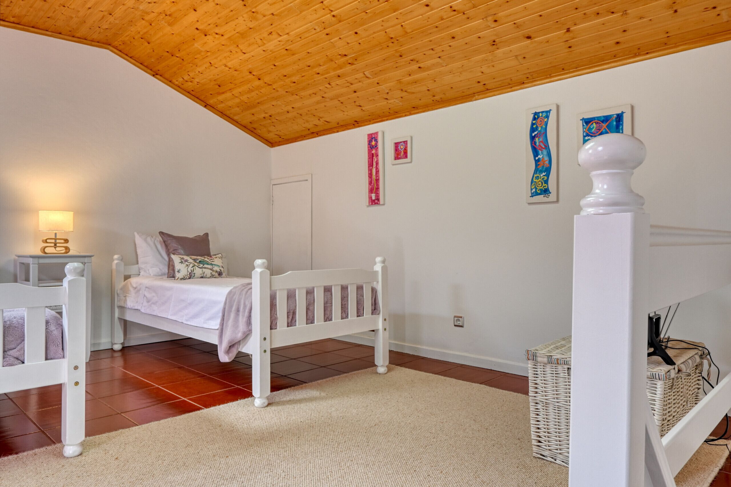 Ein Schlafzimmer mit Holzboden, einem weißen Bett, einem Nachttisch, einer Lampe und Kunstwerken an der Wand.