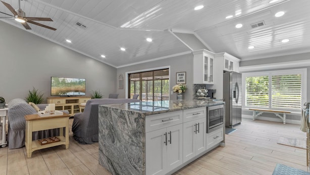 A modern kitchen with a marble island, white cabinetry, and a built-in oven.