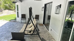 A patio area with a round table and wicker chairs, a swing set, and a ceiling fan.