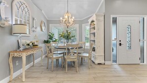 A dining area with a round table, chairs, a chandelier, and a white door with decorative glass panels.