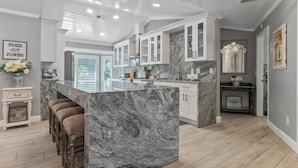 A modern kitchen with marble countertops, white cabinetry, and a central island with bar stools.