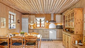 A wooden cabin interior with a dining area, kitchen, and a cabinet with glass doors.