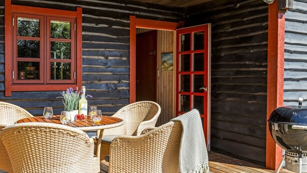 A wooden cabin with a deck, wicker furniture, a grill, and a bottle of wine.