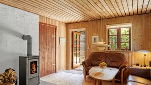 A cozy cabin interior with a wood-burning stove, a leather sofa, and a dining table.