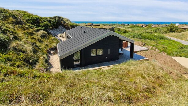 A modern black house with a sloped roof, surrounded by grassy dunes and a clear view of the ocean. - "Kristiina" - 500m from the sea by Interhome (Saltum)