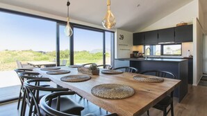 A modern kitchen with a large island, a dining area with a wooden table and chairs, and a view of the landscape. - "Kristiina" - 500m from the sea by Interhome (Saltum)