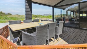 An outdoor dining area with a wooden deck, wicker chairs, and a glass-enclosed space with a view of the landscape. - "Kristiina" - 500m from the sea by Interhome (Saltum)