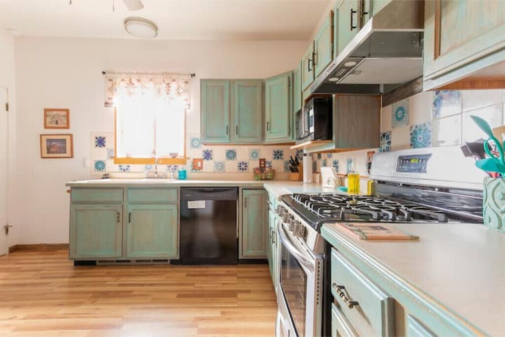 Una cocina con gabinetes color turquesa, una estufa y un lavavajillas.