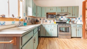 A kitchen with teal cabinets, a microwave, an oven, and a wooden countertop.