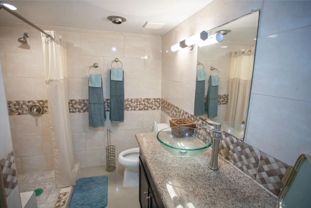 A bathroom with a glass sink, a shower, and a toilet.