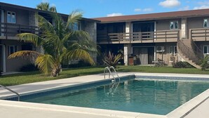 Ein modernes Gebäude mit Pool, umgeben von Palmen und blauem Himmel.
