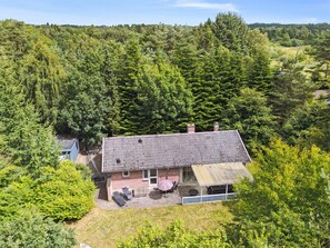 Une maison avec un toit en pente, une terrasse avec des meubles d’extérieur et une vue sur une zone boisée.