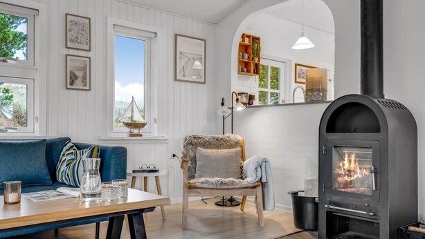 Ett mysigt vardagsrum med en öppen spis, en blå soffa, ett matbord och en bokhylla.