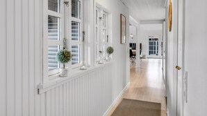 En hall med vitmålade panelväggar, flera fönster och en dörr som leder till ett annat rum.