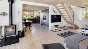 Una sala de estar moderna con una estufa de leña, un comedor, una cocina y una escalera.