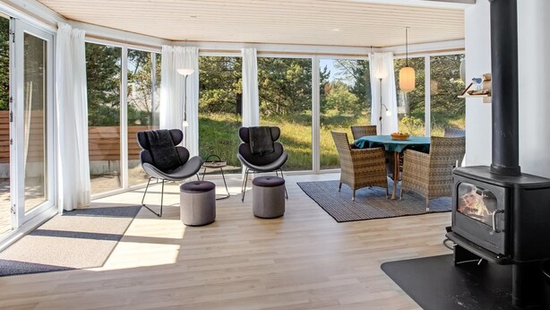 Un espacio habitable moderno y de planta abierta con estufa de leña, ventanas amplias y vistas al exterior.