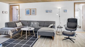 Una sala de estar moderna con un sofá gris, una mesa de centro redonda y un sillón gris. Hay cuadros enmarcados en la pared y una lámpara de pie.