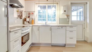 Une cuisine moderne avec des meubles blancs, une hotte de cuisinière en acier inoxydable, une fenêtre donnant sur les arbres et un lave-vaisselle encastré.
