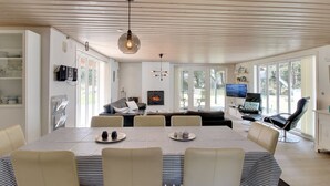 Un espace de repas moderne comprenant une grande table, plusieurs chaises, une cheminée et un téléviseur.