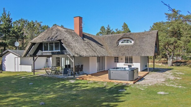 Une maison avec un toit de chaume, un jacuzzi et une terrasse couverte.