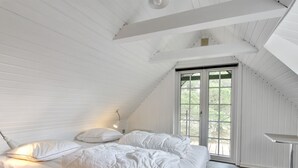 Une chambre à coucher avec un lit, des oreillers, une lampe de chevet et une fenêtre donnant sur un paysage verdoyant.