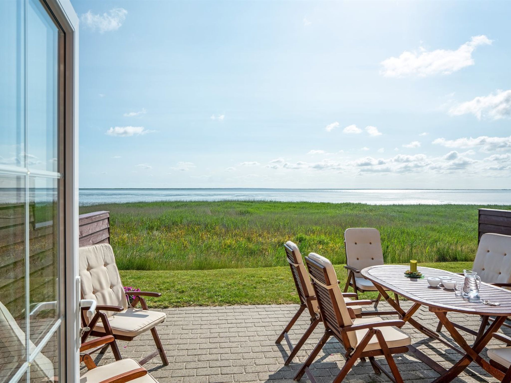 A patio with a table and chairs overlooking a grassy field and the sea.
