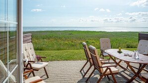 En terrasse med bord og stole med udsigt over en græsplæne og havet.