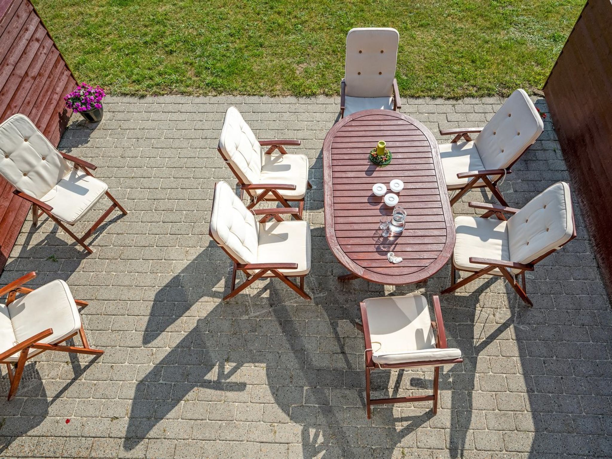 Una terrazza esterna con un tavolo rotondo in legno, circondato da sei sedie bianche imbottite con struttura in legno.
