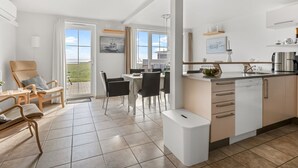 Et moderne køkken med en central ø, et spiseområde med bord og stole, samt et opholdsområde med stol og bænk.