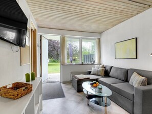 Un salon moderne avec un canapé gris, une table basse en verre et un téléviseur fixé au mur.