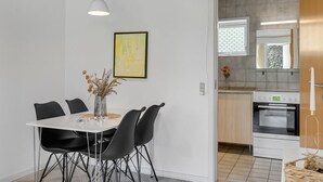 A modern kitchen with white cabinets, a built-in oven, and a dining area with a white table and black chairs. - "Skarthi" - 20km from the sea by Interhome (Skærbæk)