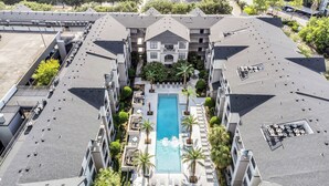 Um hotel moderno com piscina central, várias varandas e um jardim bem cuidado.