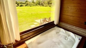 Una stanza con una vasca da bagno ampia, un pavimento in legno e vista su un campo verde attraverso una finestra.