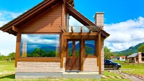 Una piccola baita di legno con fondamenta in mattoni, ampie finestre e un portico coperto.