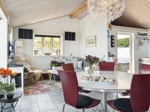 Un vaste espace de vie comprenant un coin repas avec une table, des chaises rouges et une cuisine visible au fond.