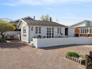 Un bâtiment blanc avec un toit en pente, une terrasse dotée de sièges extérieurs et un petit jardin.