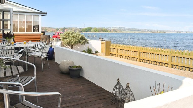 A wooden deck with outdoor seating, a white wall, and a view of the water. - "Tameka" - 10m to the fjord by Interhome (Munkebo)