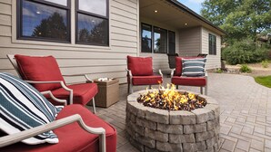 A patio area with a stone fire pit surrounded by red and white cushioned chairs. - Cozy Retreat Family Home (Klamath Falls, OR)
