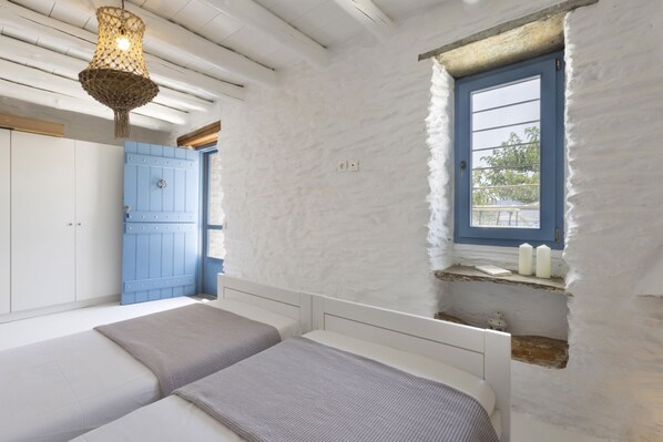 Un dormitorio con dos camas, una puerta azul, un ventanal y una lámpara colgante.